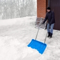 Mężczyzna odśnieżający podjazd dużym pługiem w kolorze niebieskim, który można kupić w naszym sklepie