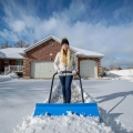 Kobieta odśnieżający podjazd dużym pługiem w kolorze niebieskim, który można kupić w naszym sklepie